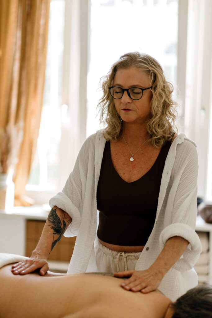 Heike Wangler legt beide Hände auf den oberen und unteren Rücken einer Klientin und arbeitet energetisch in meditativem Fokus