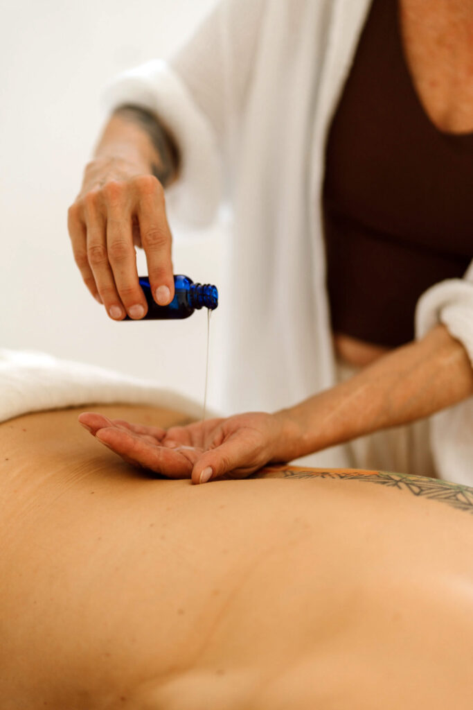 Heike Wangler gießt Massageöl in ihre Handfläche über dem Rücken einer Klientin